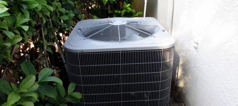 ac condenser unit installed outside a home near shrubs